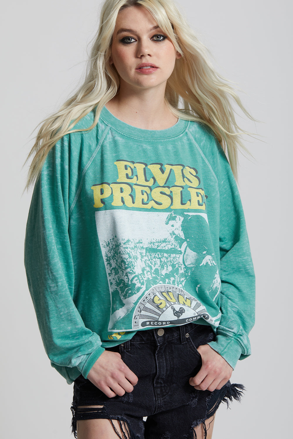 Person wearing a green 'Elvis Presley' sweatshirt with a graphic design on a plain background
