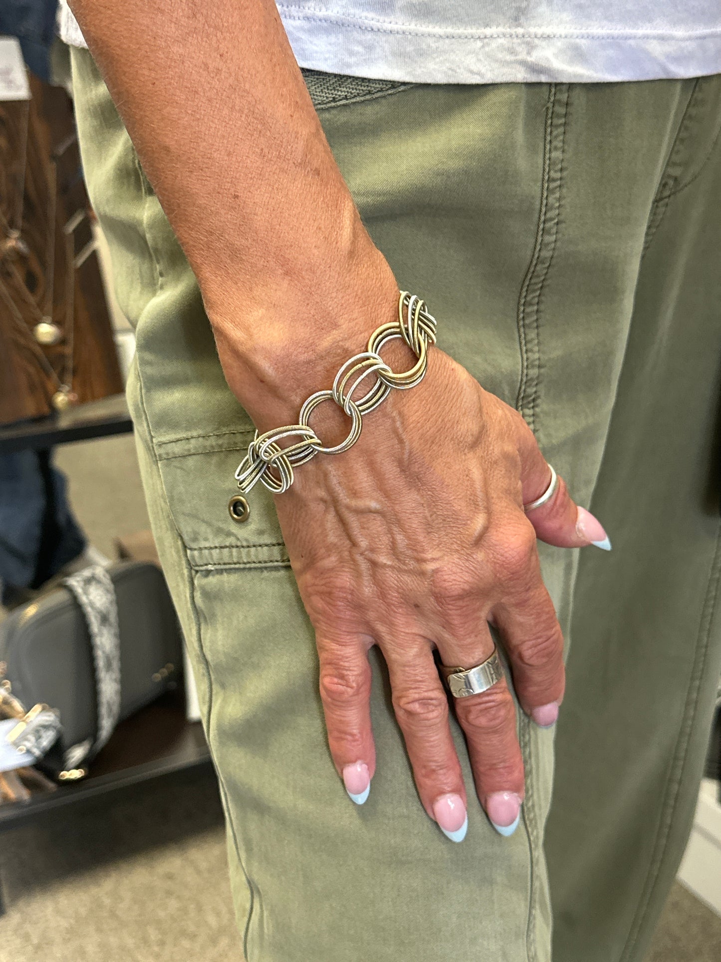Hand wearing a silver bracelet and ring on a green jacket background