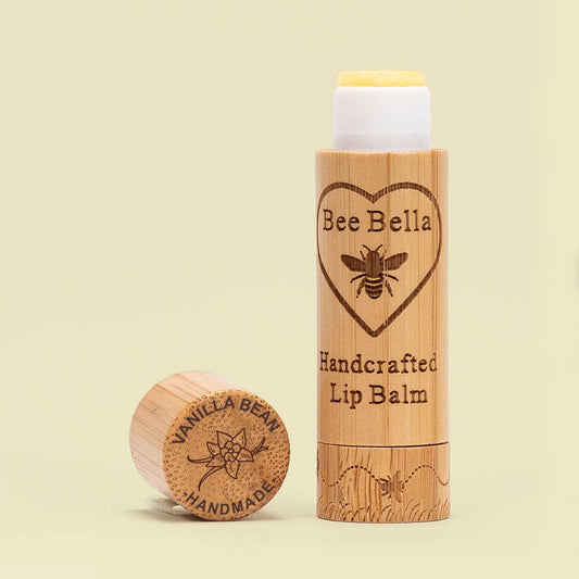 A tube of Bee Bella handcrafted lip balm in pumpkin spice flavor, placed next to a piece of sustainably sourced bamboo which is not pictured.