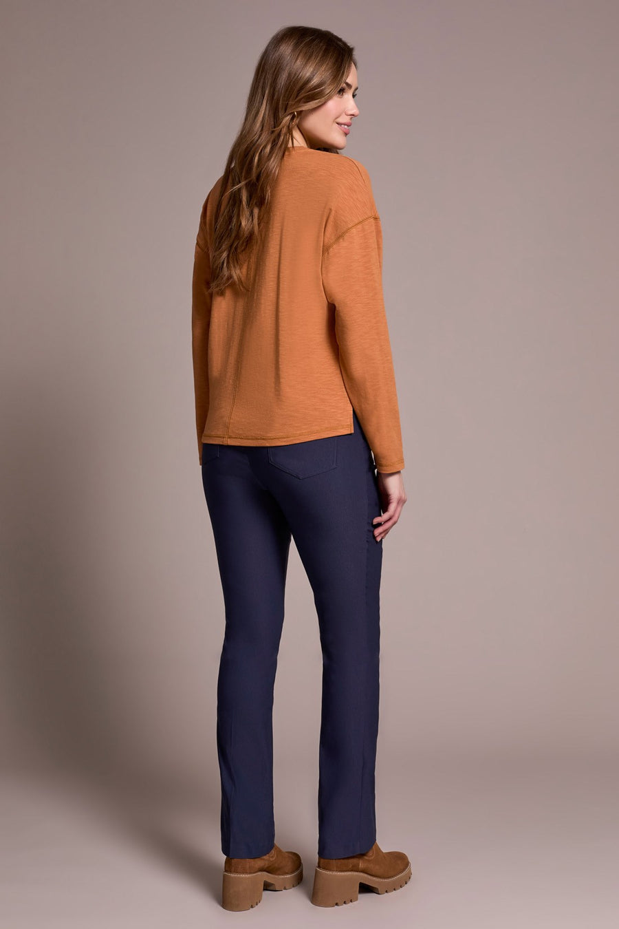 Woman wearing a brown sweater and blue pants against a beige background