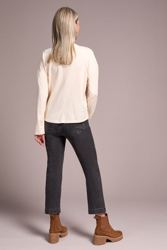 Person wearing a cream sweater and dark jeans with brown boots on a plain background