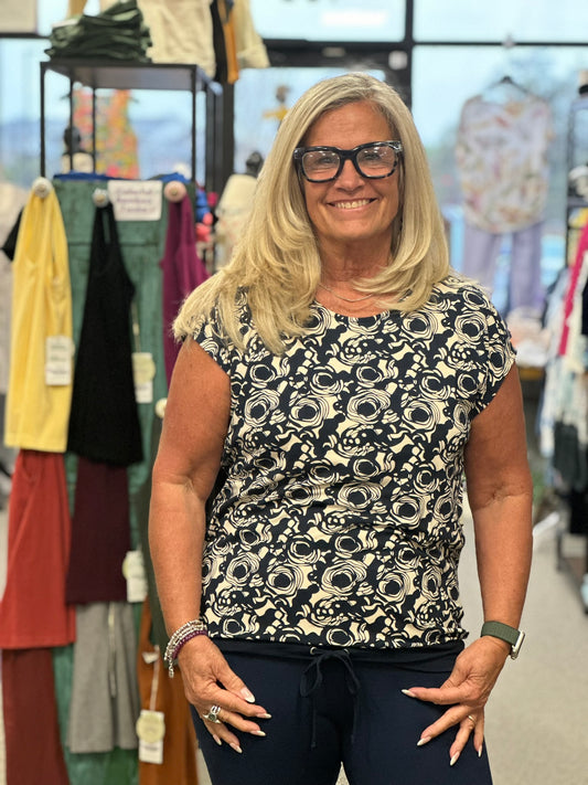 Lively print swirl top with a cap sleeve and adjustable hemline. This will match a skirt we carry or go with just about anything in your wardrobe. Even though the color is navy, it looks great with black as well.